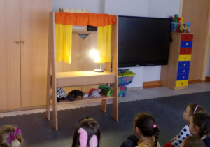 Dzieci obserwujące oświetloną scenkę teatrzyku.
